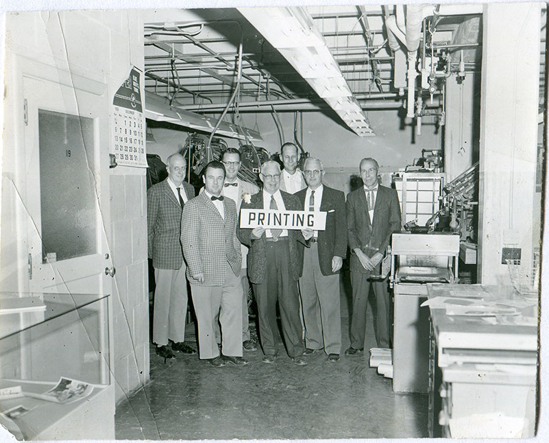 Men hold a sign that says 'printing' in the Shakespeare Press Museum.